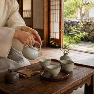 Pouring tea from a celadon teapot at a low wooden table in the hanok tea room